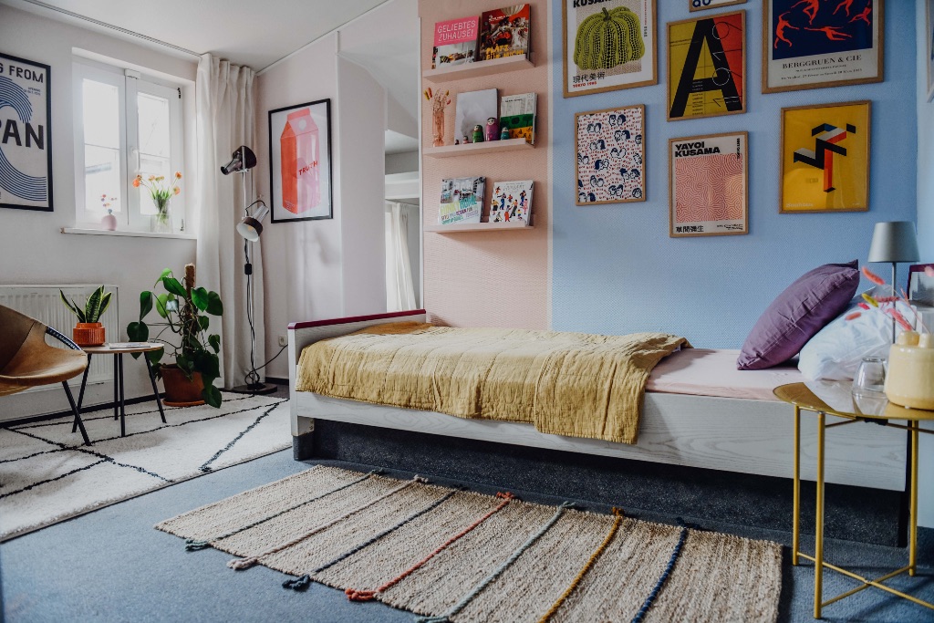 sleepArt room for 3 · room overview with bed in front of blue-pink wall and poster gallery